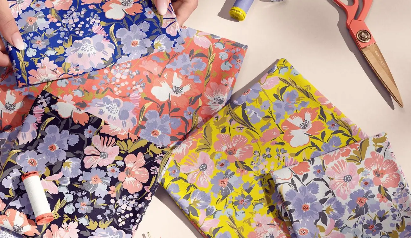 Floral-patterned jersey fabrics arranged in a styled flat-lay with scissors, thread and a measuring tape.